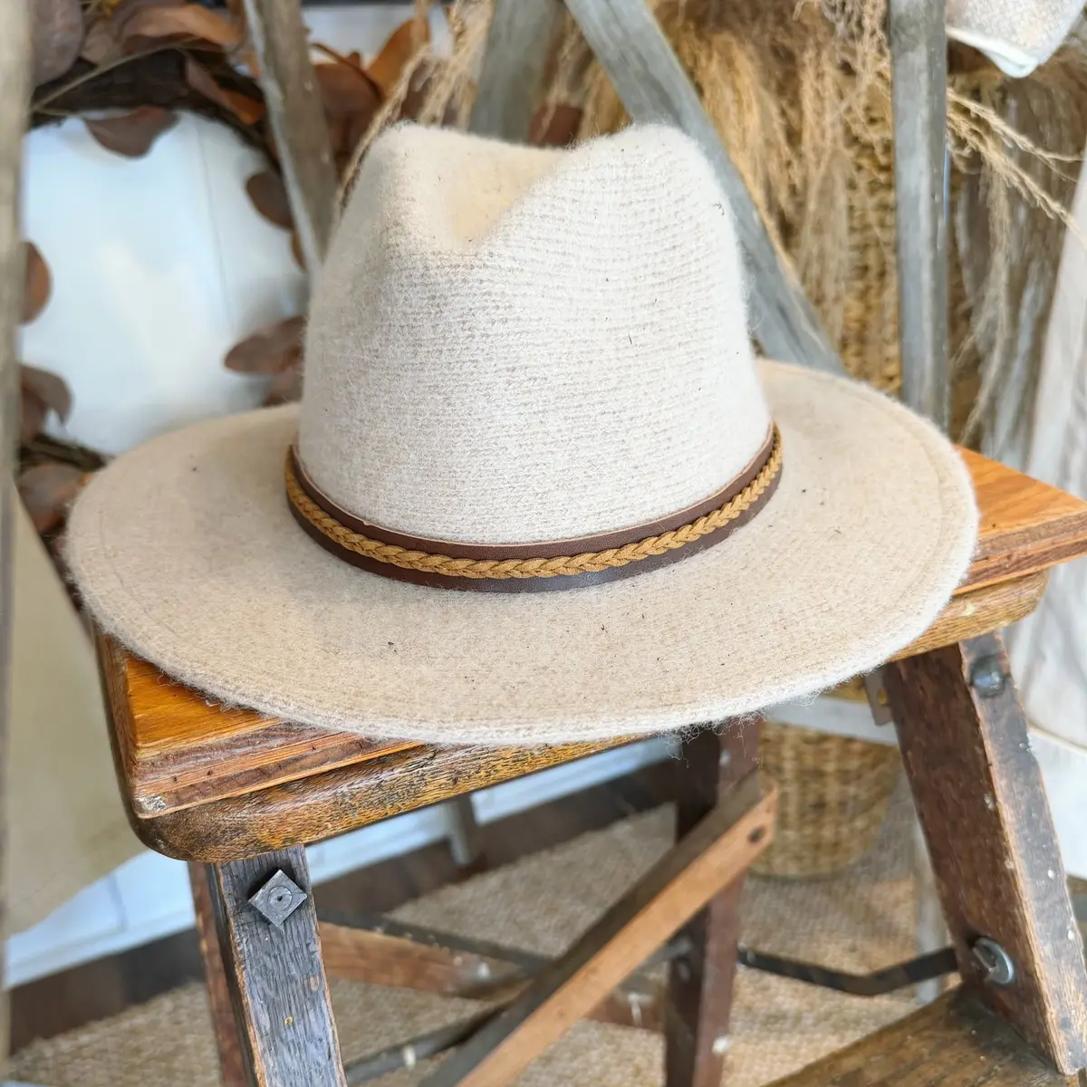 Cream felt fedora with a braided band on a wooden stool