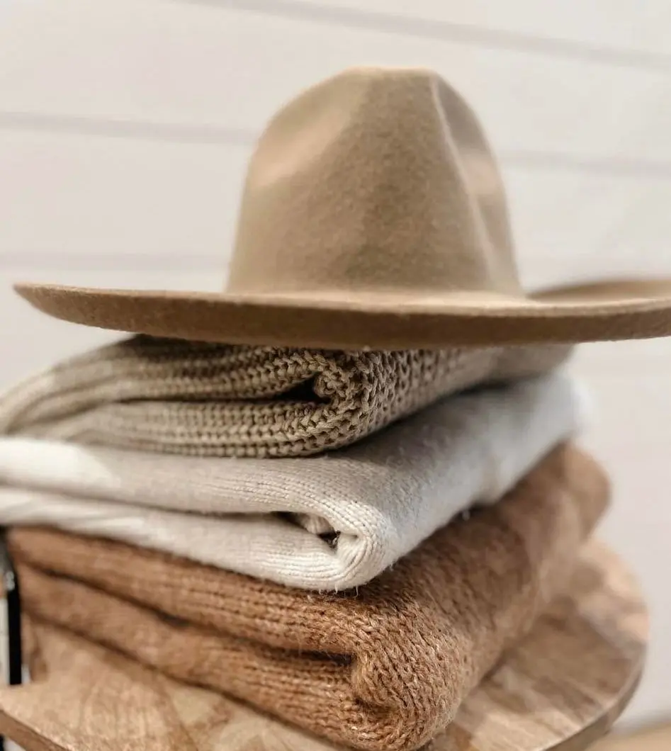 Taupe felt hat resting on a stack of folded oat and camel sweaters