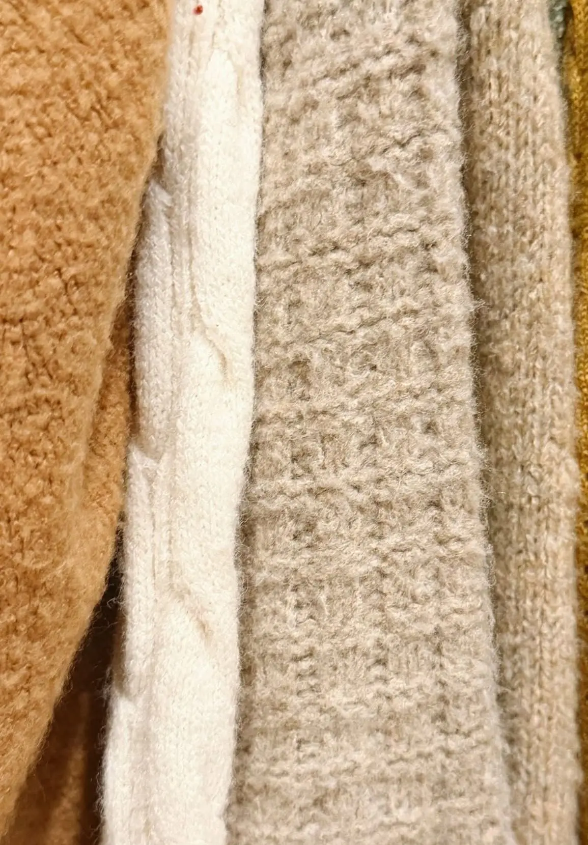 Close-up of oat, cream and camel knit sweaters on the rail