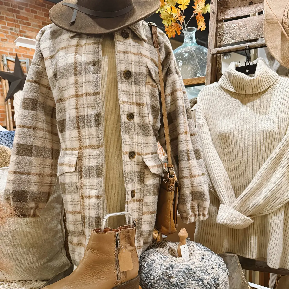 A plaid shacket, ribbed turtleneck, leather crossbody and tan ankle boots styled against the shop's old brick wall