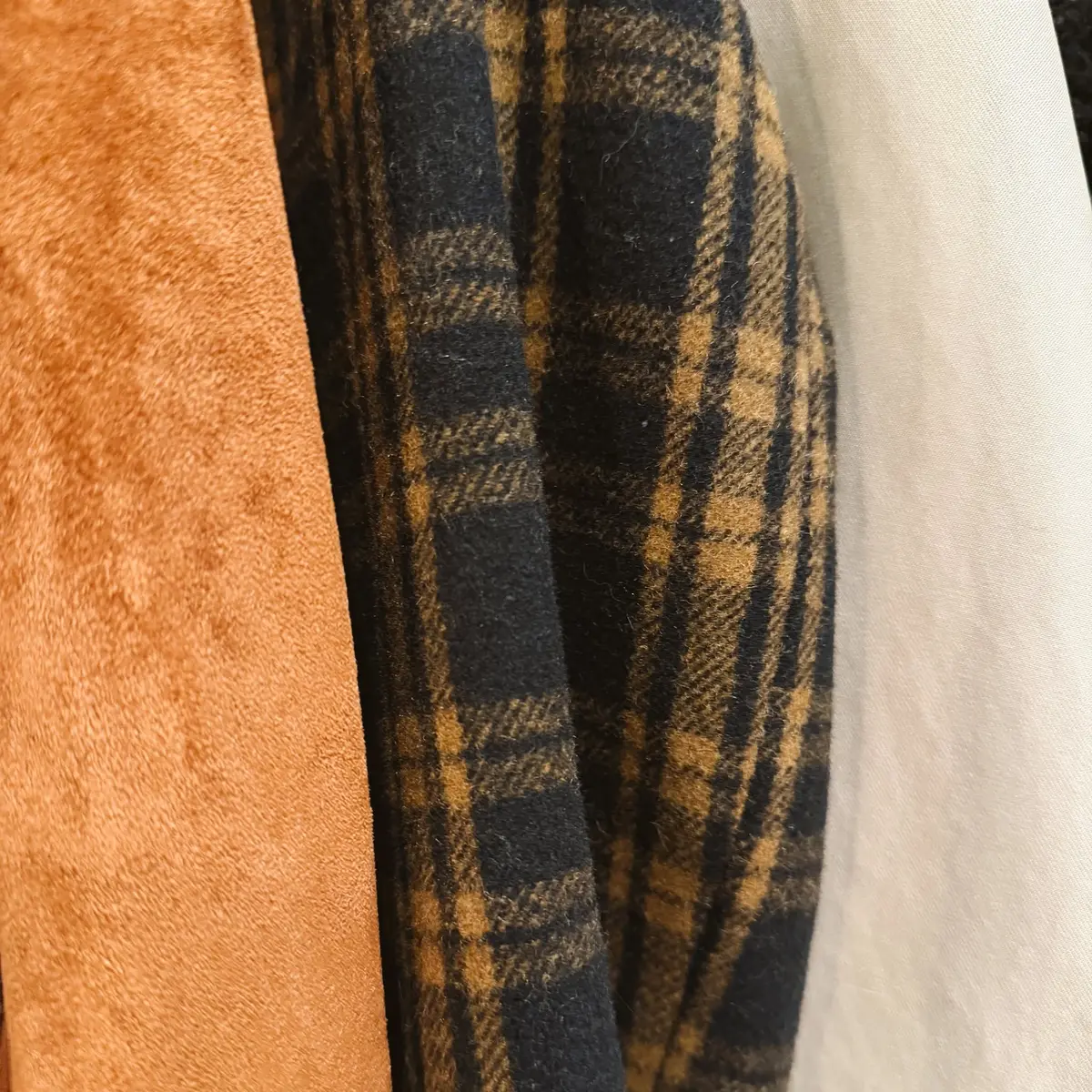 Rust suede, black and camel wool plaid and a cream coat hanging side by side